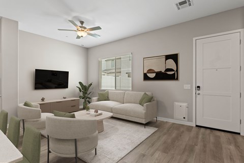 A living room with a white couch, a green cushion, a white coffee table, a white dining table, a white rug, a white ceiling fan, a flat screen TV, a plant, and a picture on the wall