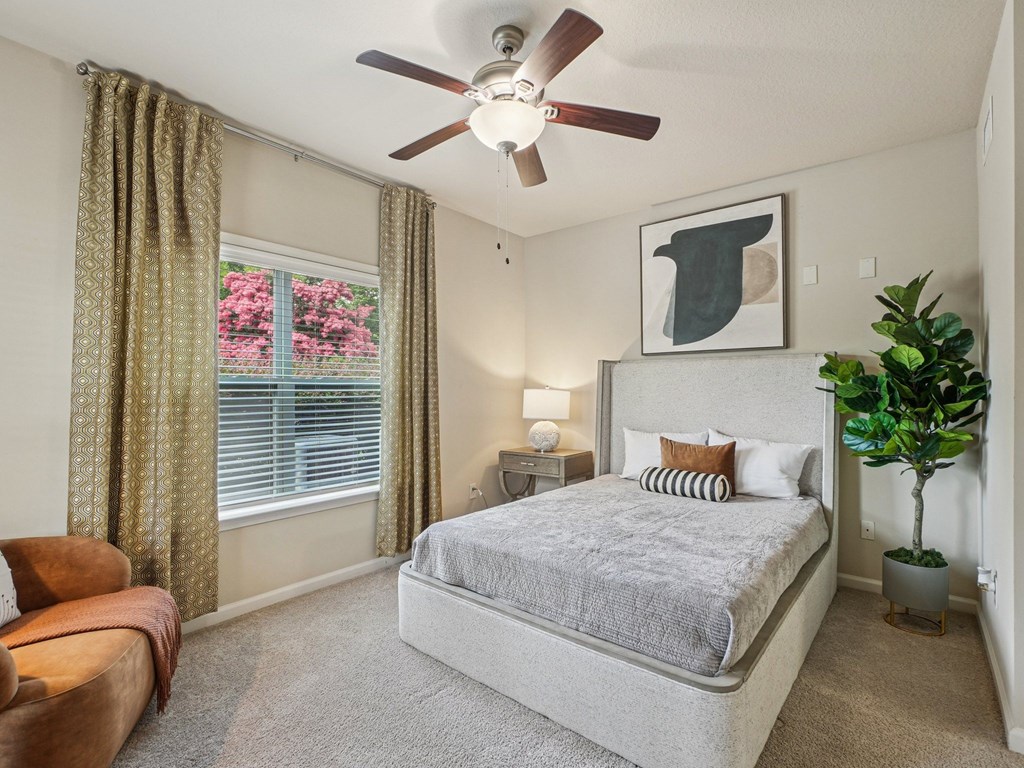 A bedroom with a bed, a couch, a ceiling fan, and a plant.