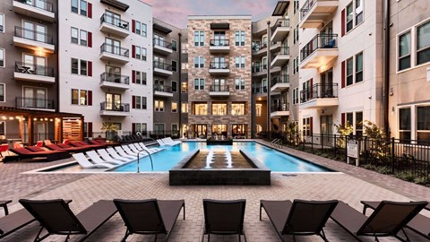 A swimming pool surrounded by lounge chairs in front of apartment buildings.