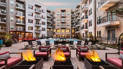 A fire pit in the middle of a courtyard surrounded by chairs and buildings.
