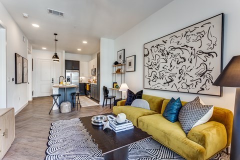 A living room with a yellow couch and a black and white abstract painting on the wall.
