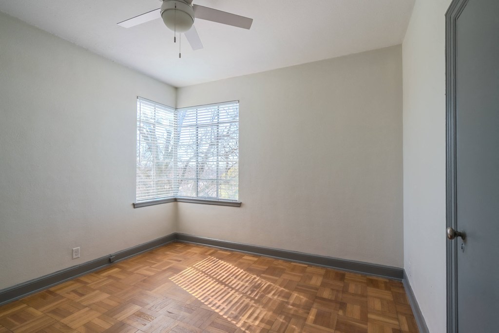 an empty living room with wood floors and a window and a ceiling fan