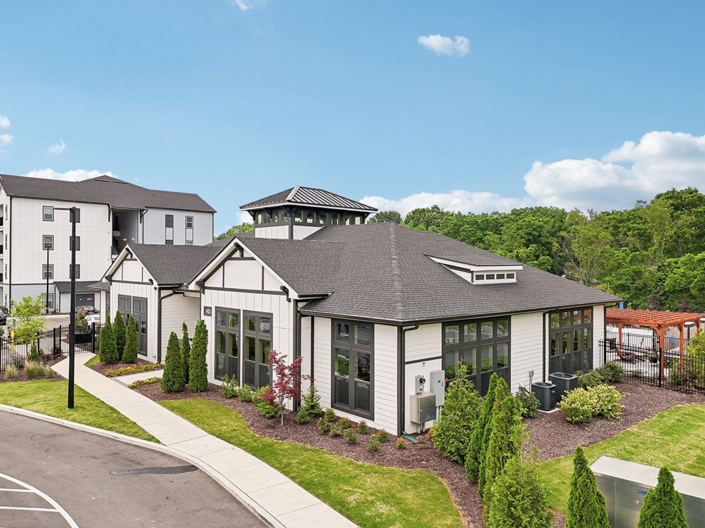 A white building with a black roof is surrounded by greenery.