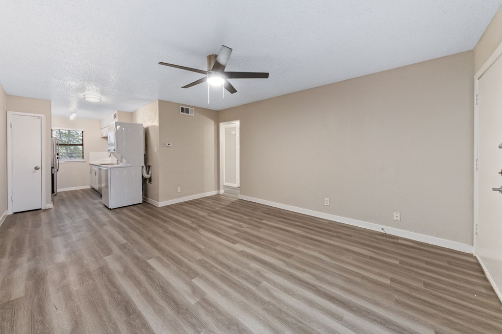 a living room with a ceiling fan and a kitchen in the background