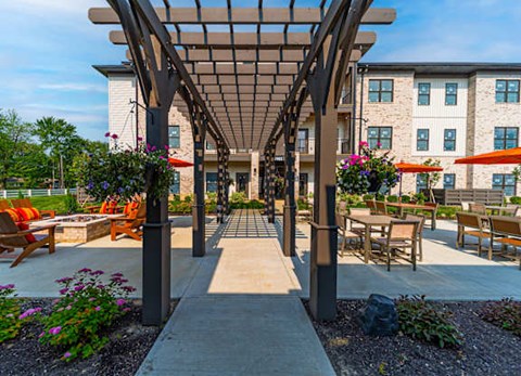 A covered walkway with benches and flowers leading to a building.