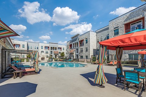 A pool area with a striped umbrella and chairs.