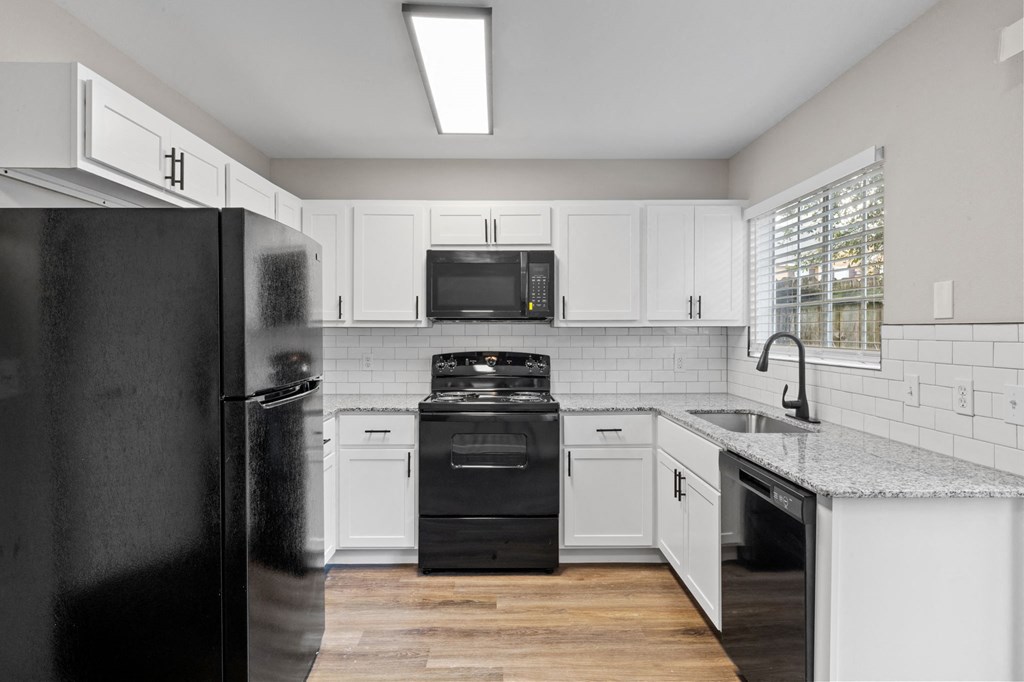 A black refrigerator is in a kitchen with white cabinets.