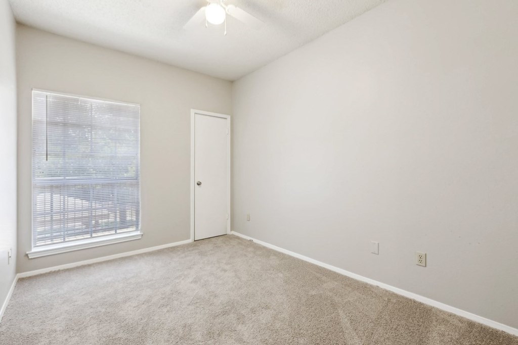A room with a carpeted floor and a window with blinds.
