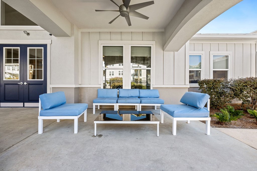 A white patio with blue cushions and a fan.