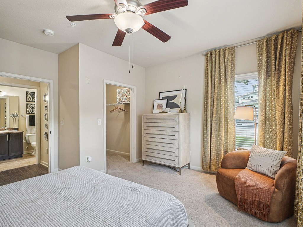 A bedroom with a bed, chair, and a ceiling fan.