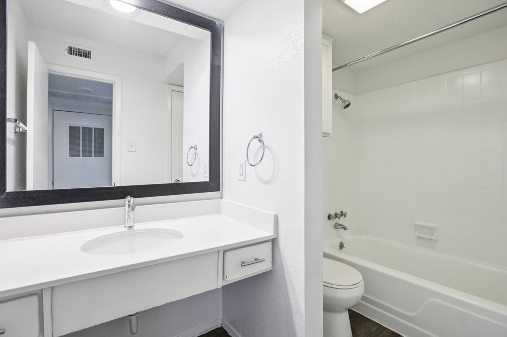 A white bathroom with a sink, mirror, toilet and bathtub.