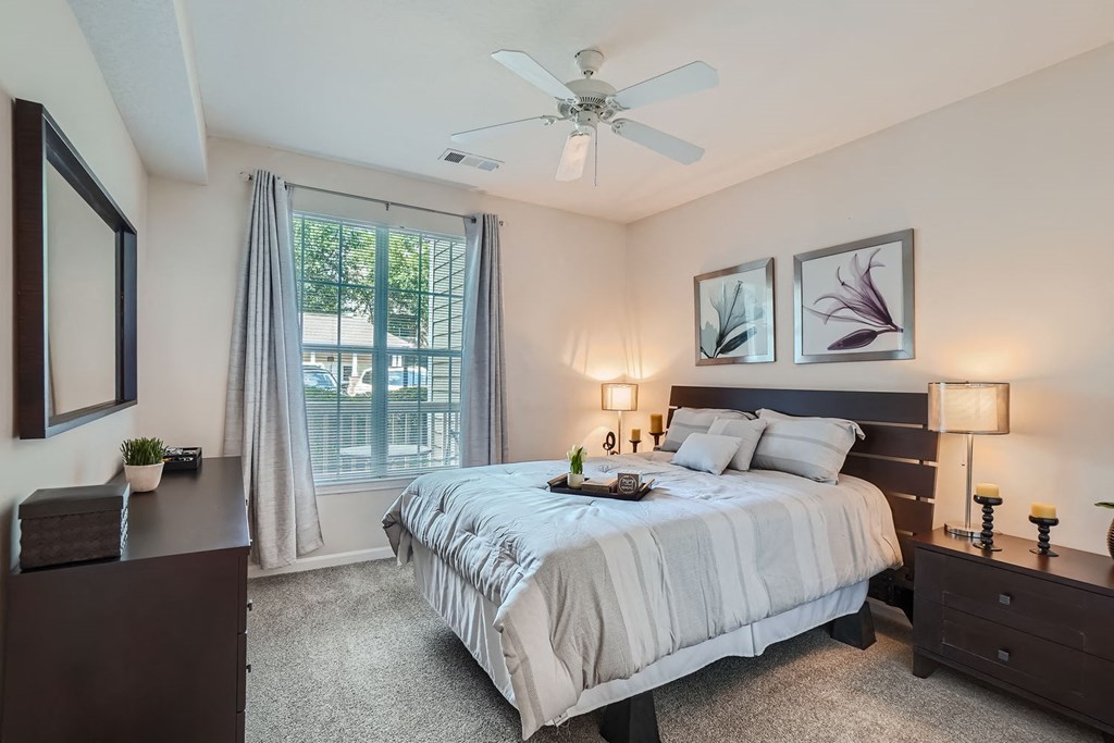A bedroom with a large bed, a ceiling fan, and a window with curtains.