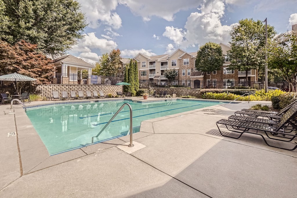 A swimming pool surrounded by a stone wall and lounge chairs.