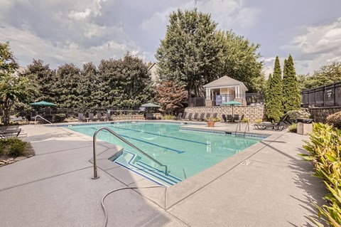 A large outdoor swimming pool surrounded by trees and a gazebo.