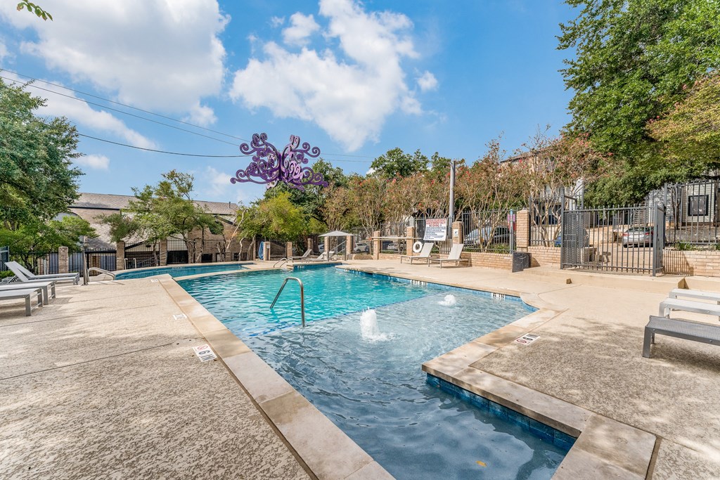a swimming pool with a fountain and a fence with trees