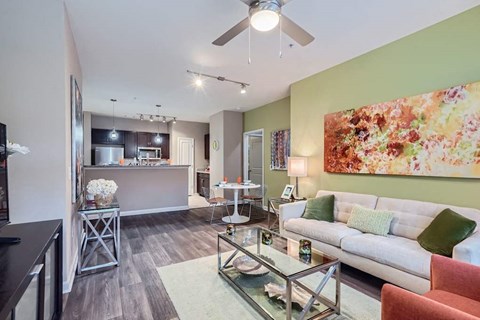 A living room with a glass coffee table and a painting on the wall.