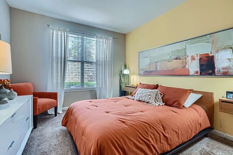A bedroom with a bed, a chair, and a painting on the wall.
