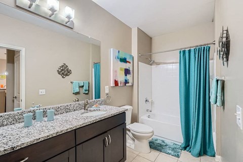 A bathroom with a white toilet, a sink with a mirror above it, and a shower with a blue curtain.