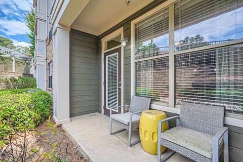 A grey wicker chair and a yellow stool are placed on a porch.