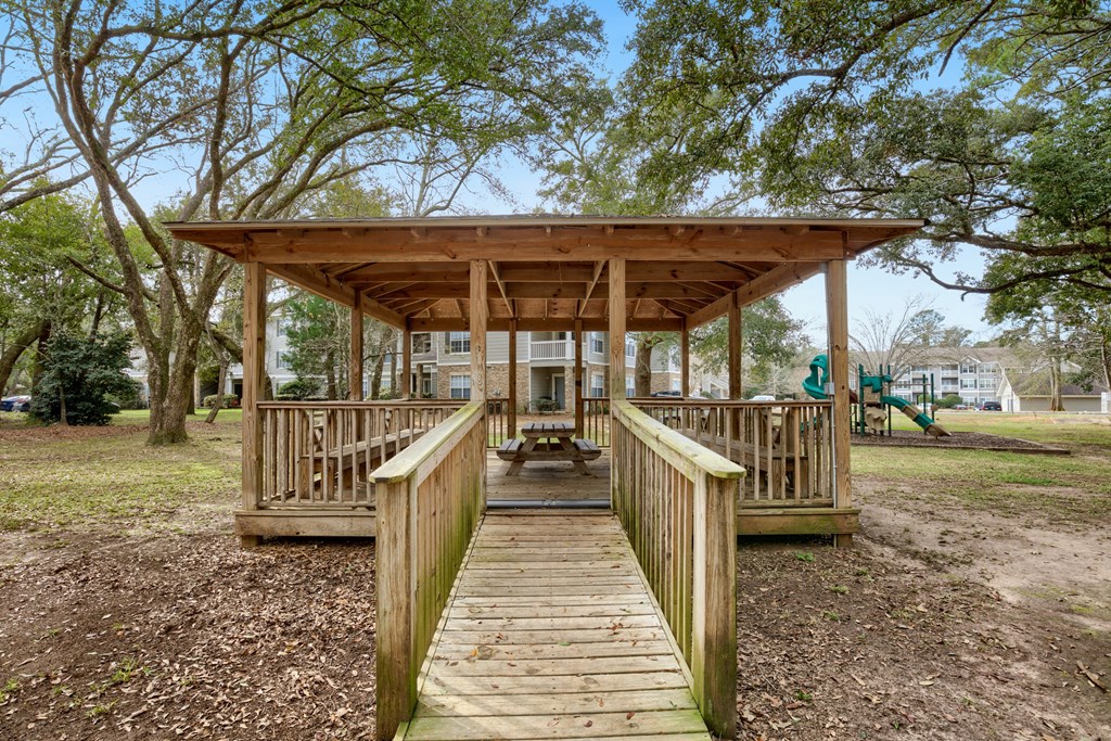 a wooden bridge leading to a pavilion with a playground in the background