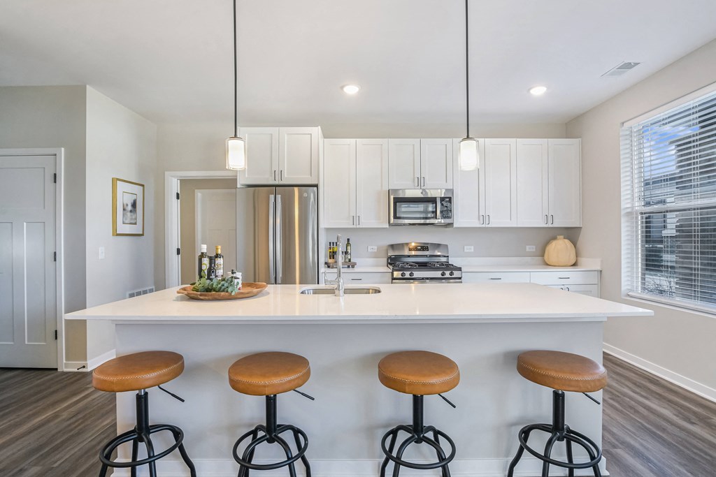A kitchen with white cabinets and a white island with four stools.