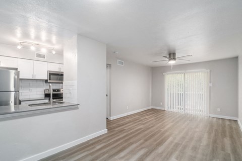an empty living room with a kitchen and a ceiling fan