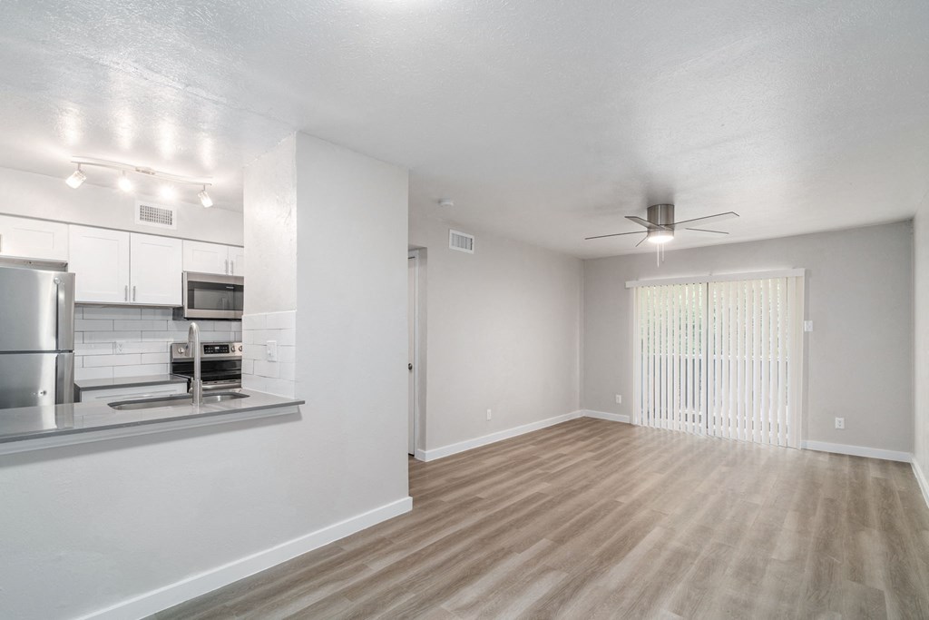 an empty living room with a kitchen in the background