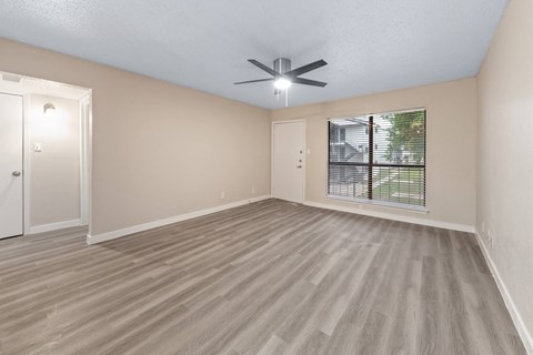 an empty living room with a ceiling fan and a window