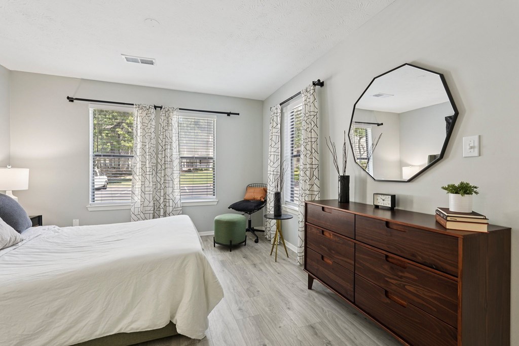 A bedroom with a bed, dresser, mirror, and window with curtains.