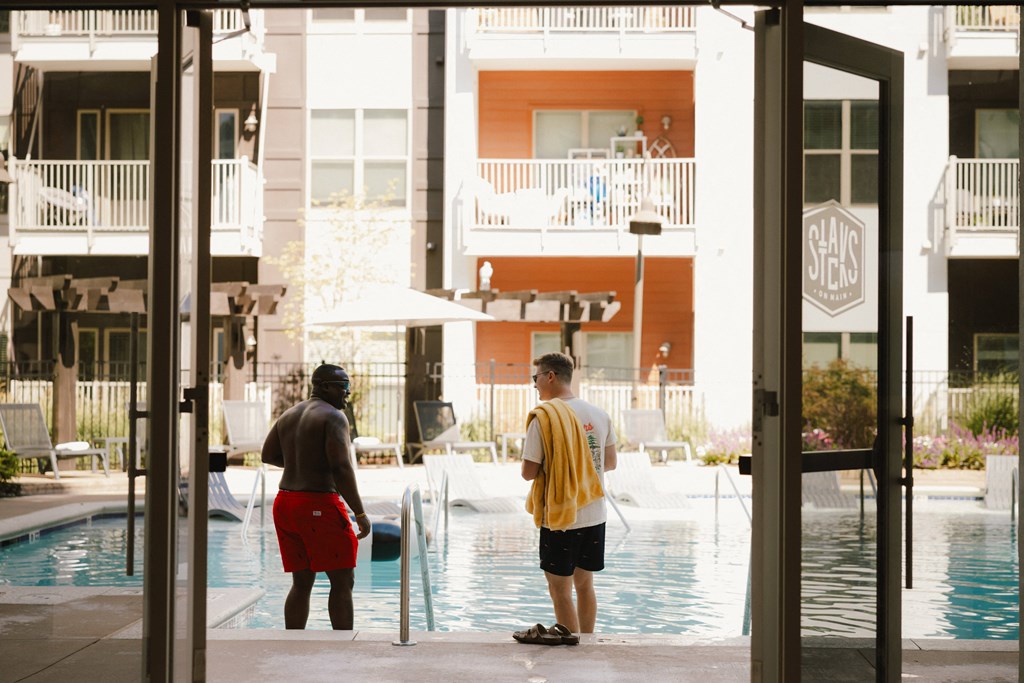 two men standing by a swimming pool in front of a building