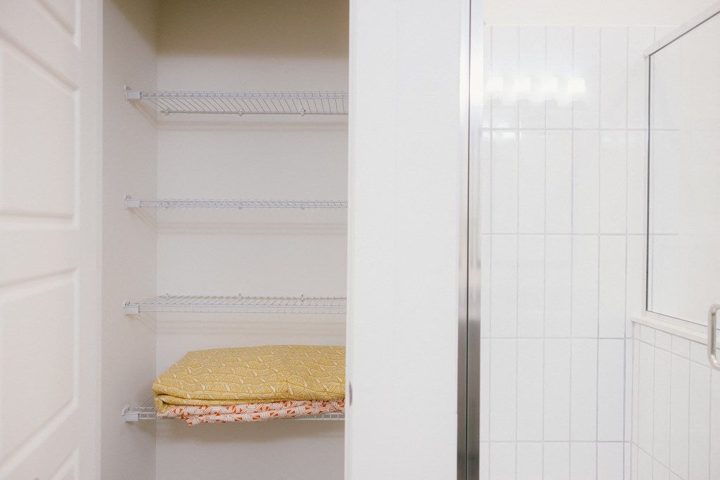 a walk in closet with white walls and white shelves and a glass closet door