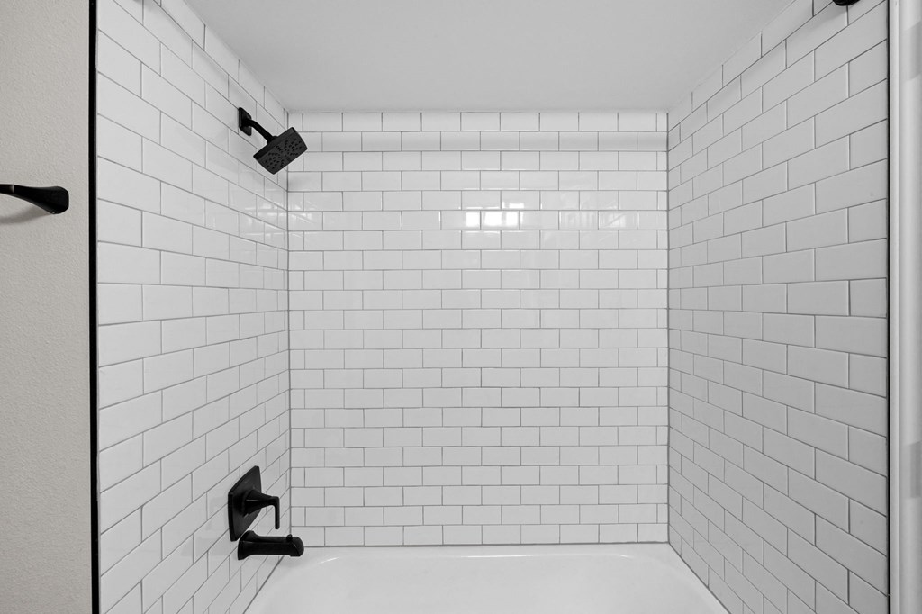 A white tiled shower stall with black handles.