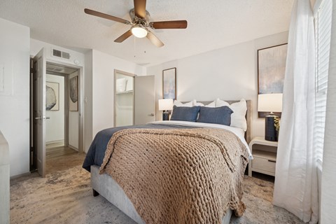 A bedroom with a bed covered in a brown blanket and a ceiling fan.