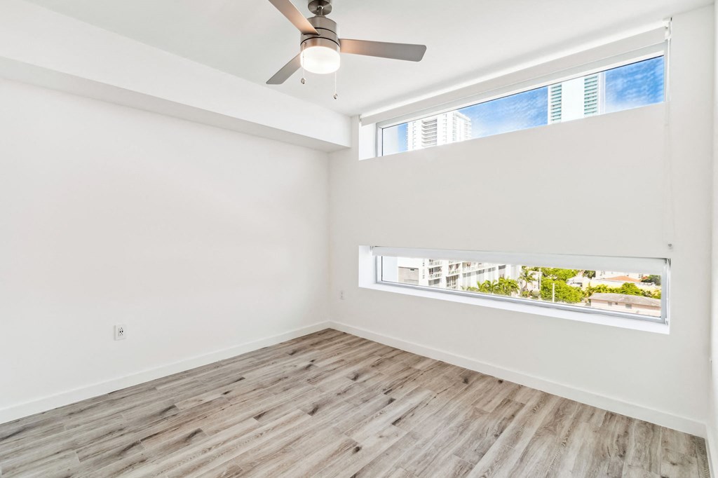 an empty room with a ceiling fan and two windows