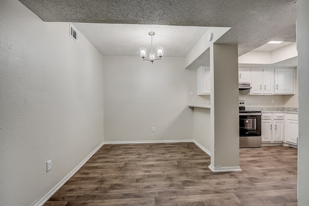 an empty living room with a kitchen in the background