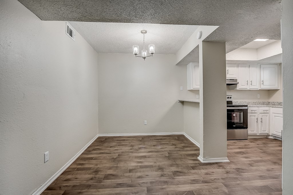 an empty living room with a kitchen in the background