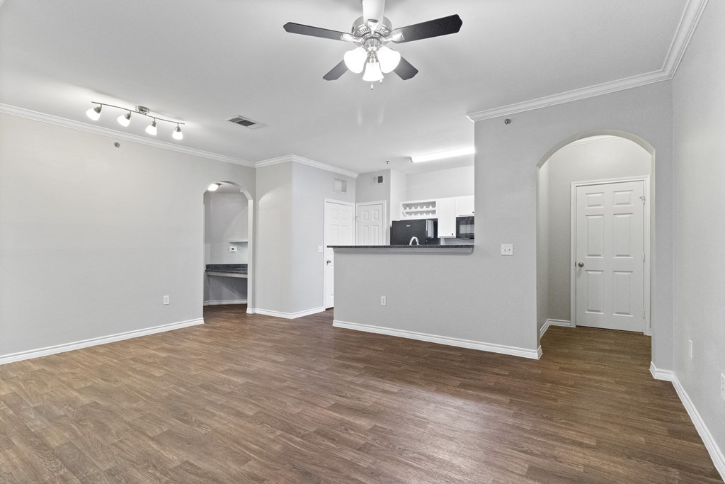 an empty living room with a ceiling fan and a kitchen