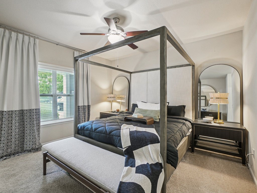 A bedroom with a four poster bed and a bench underneath it.