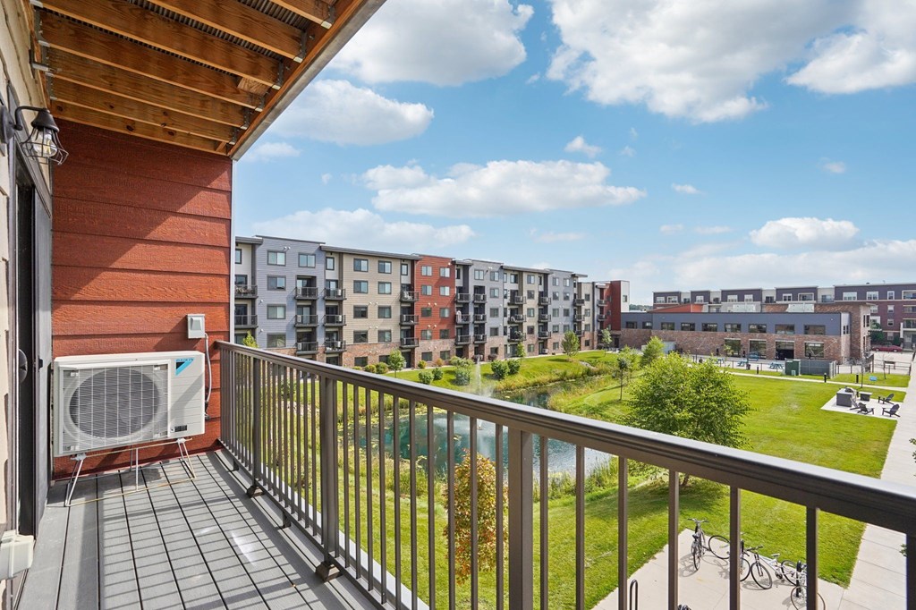 A balcony with a fan and a view of a grassy area and buildings.