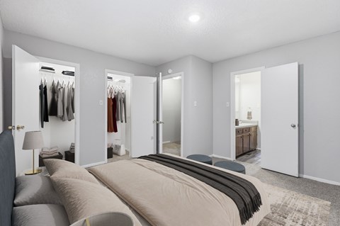 A bedroom with a large bed and a closet with clothes hanging.