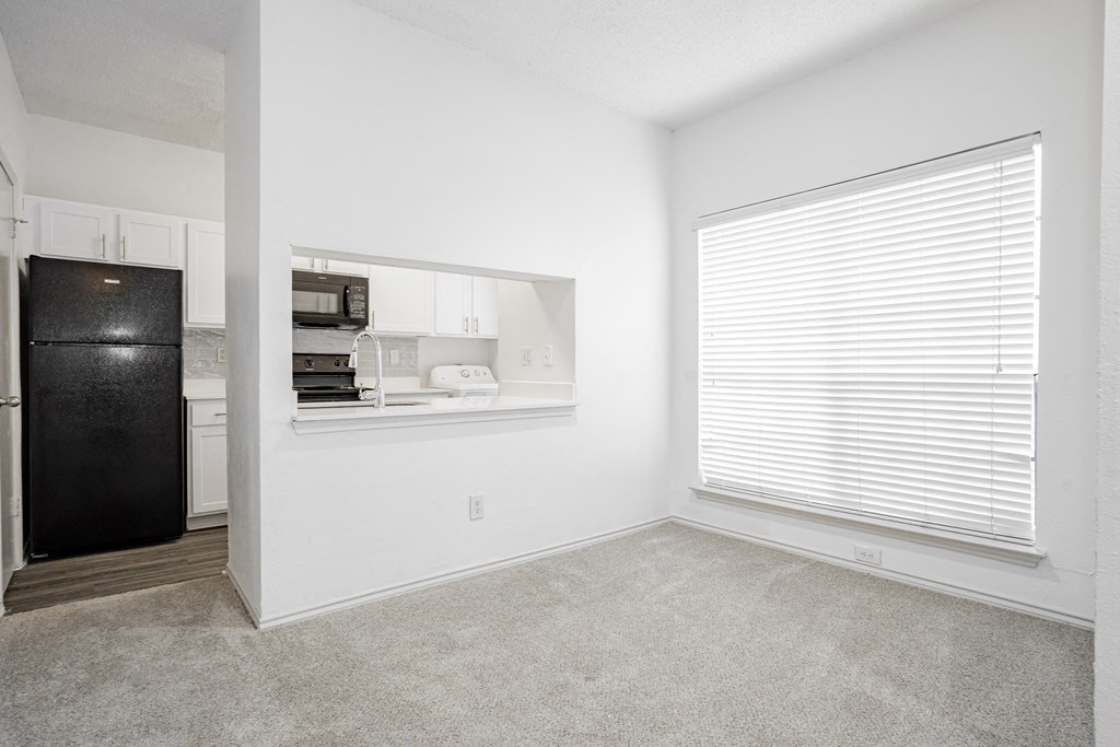an empty room with a large window and a black refrigerator