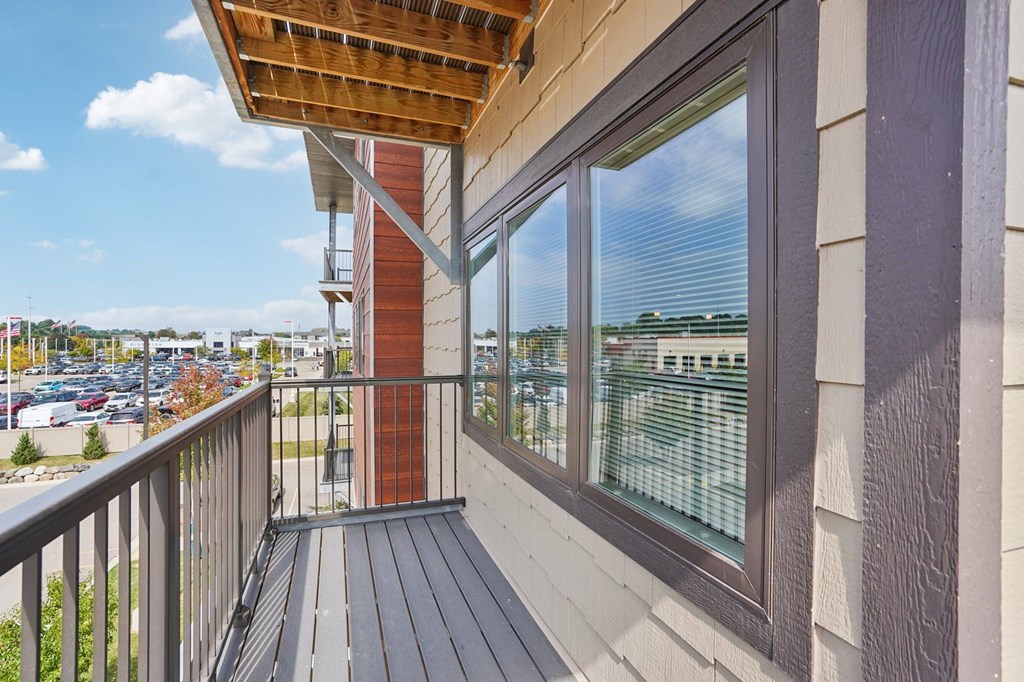 A balcony with a wooden floor and a view of a parking lot.
