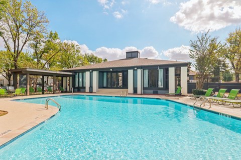 A swimming pool in front of a house with a sunny sky.