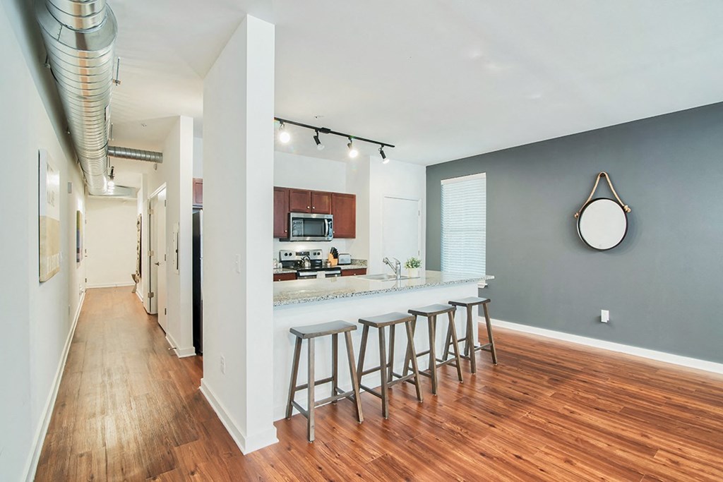 an open kitchen with a bar and stools in a living room with a hallway