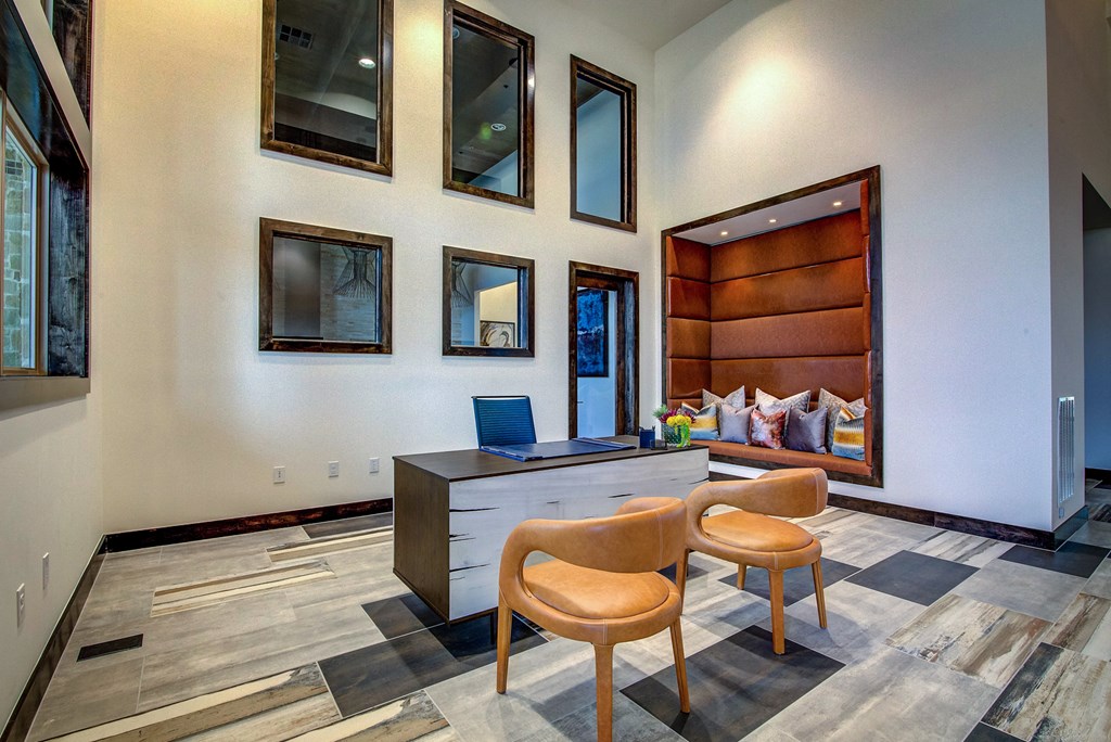 a desk with a laptop and two chairs in a large room with a bed in the background