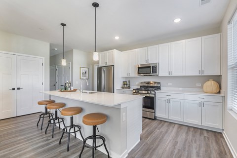 A kitchen with white cabinets and a bar area with stools.