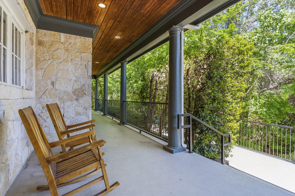 two rocking chairs on a porch with a rock wall and trees