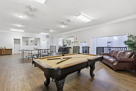 A pool table is in the middle of a room with a couch and chairs.
