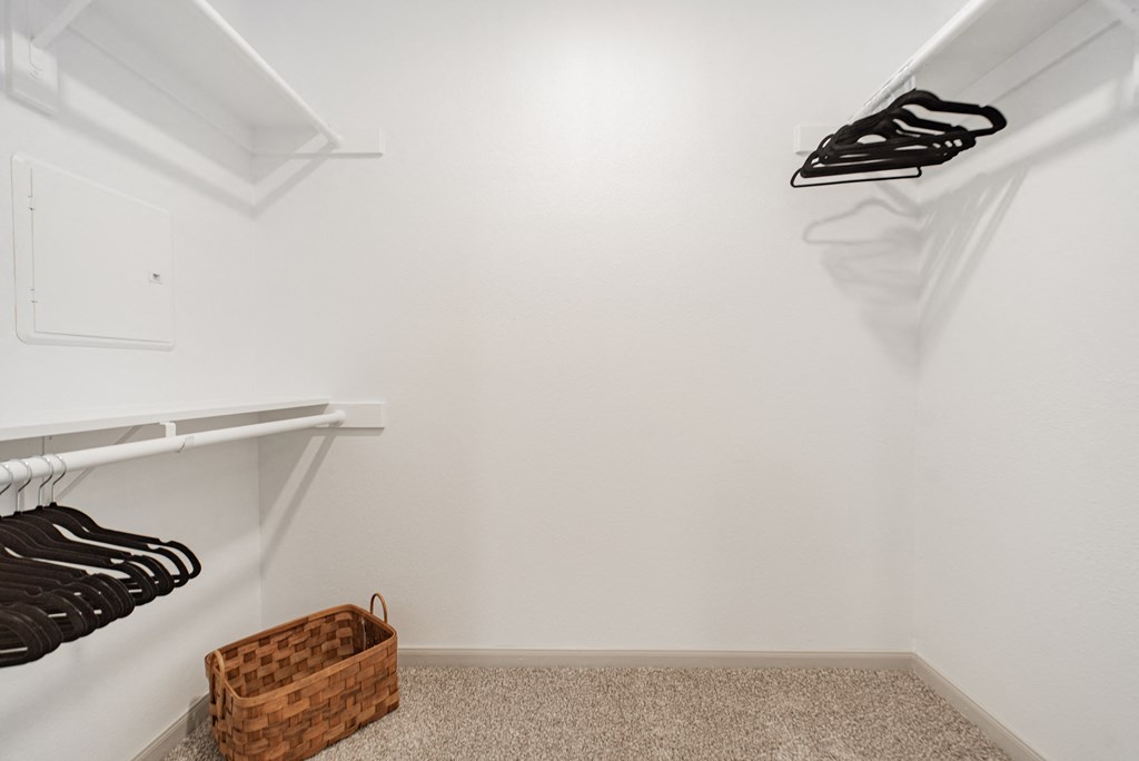 a walk in closet with white walls and shelves and a basket on the floor