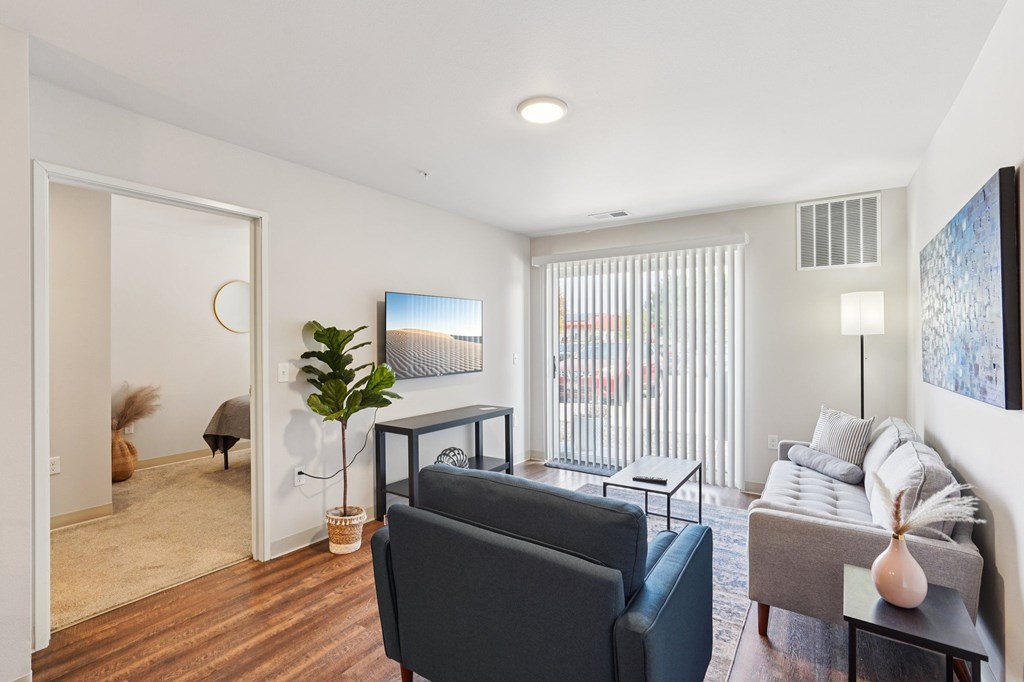A living room with a grey couch, a black chair, a wooden floor, and a painting on the wall.